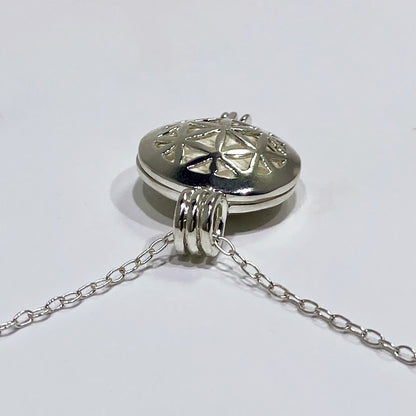 silver locket top view with a white stone inside and a chain in a. white background