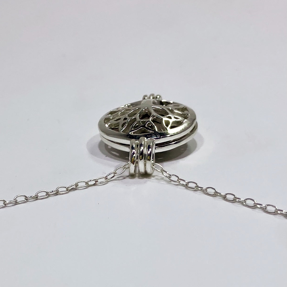 silver locket top view with a black stone inside and a chain in a. white background