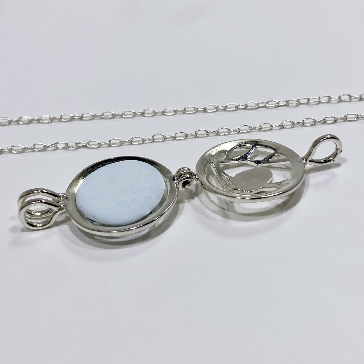 silver locket open with a light blue stone inside and a chain in a white background