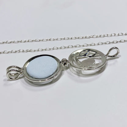 silver locket open with a light blue stone inside and a chain in a white background