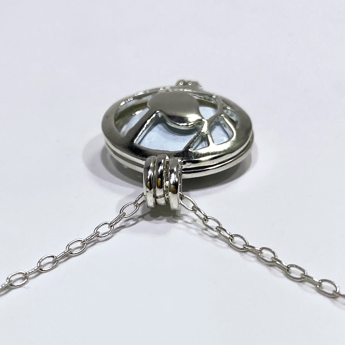 silver locket top view with a light blue stone inside and a chain in a. white background