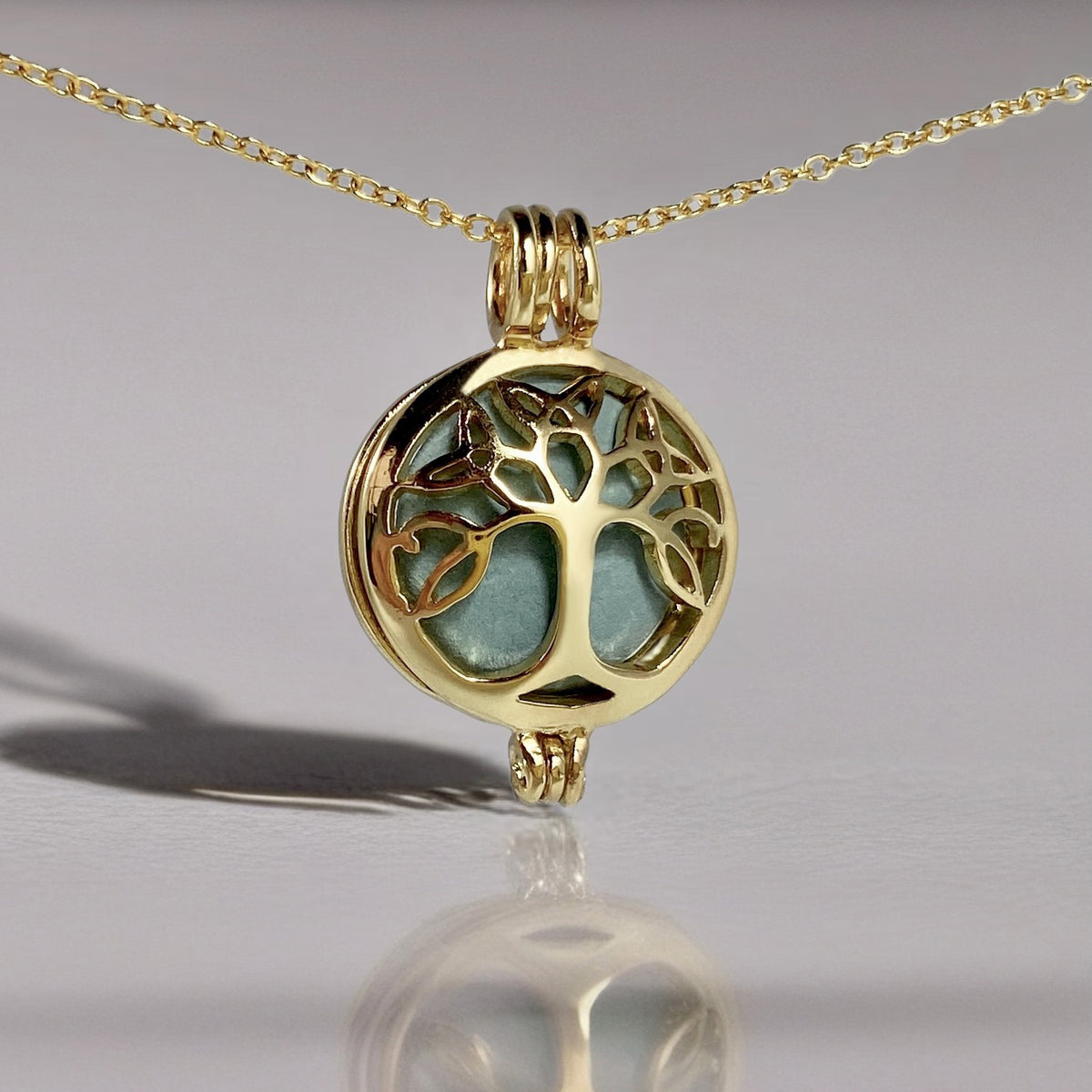 gold locket in a chain with a tree design and a green stone inside